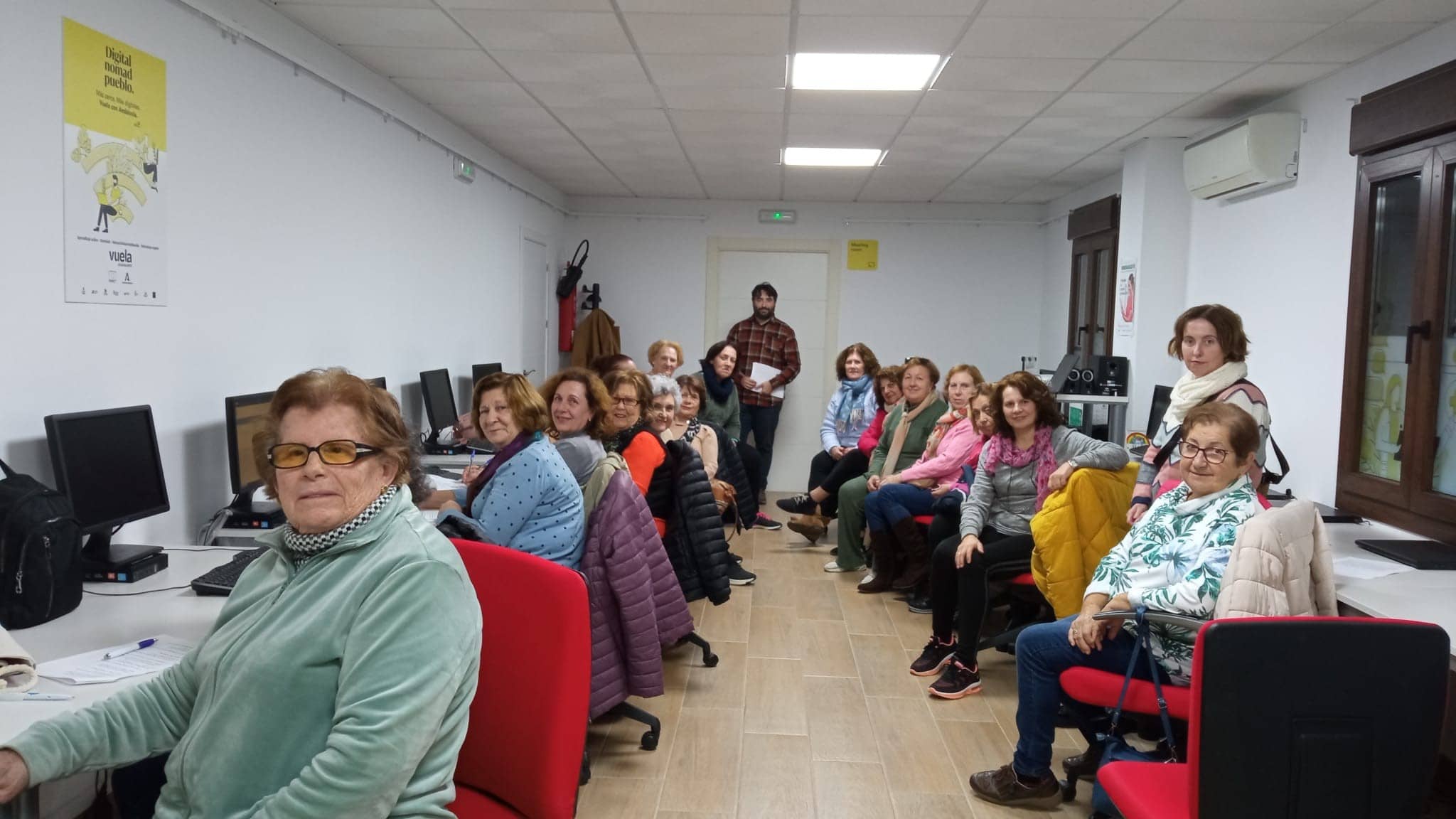 Grupo de mujeres mayores sentadas frente a mesas de ordenador y mirando a la cámara