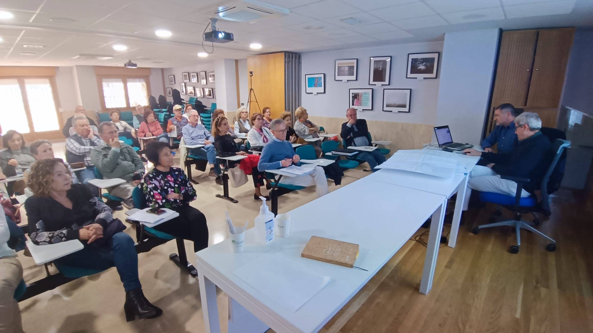 Grupo de personas mayores del proyecto senior cohousing Granada sentadas frente a una mesa donde hay dos personas con un ordenador.