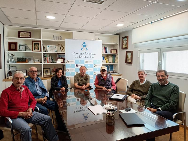 Miembros del Grupo de Trabajo de Distribución de Espacios del proyecto Residencial Josefina Castro Senior Cohousing reunidos en una sala del Consejo Andaluz de Enfermería, sentados alrededor de una mesa, con documentos y una pancarta institucional de fondo
