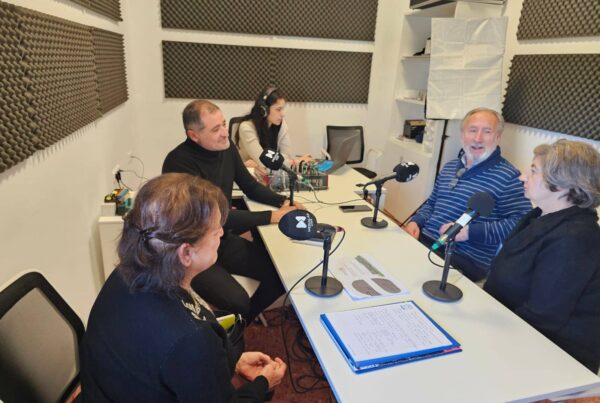 La imagen muestra al presidente de Hábitat Colaborativo y dos personas socias del Residencial Josefina Castro en una sala de grabación, sentadas alrededor de una mesa blanca con micrófonos. En el fondo, se observan paneles de insonorización en las paredes. Una persona está frente a una consola de audio.