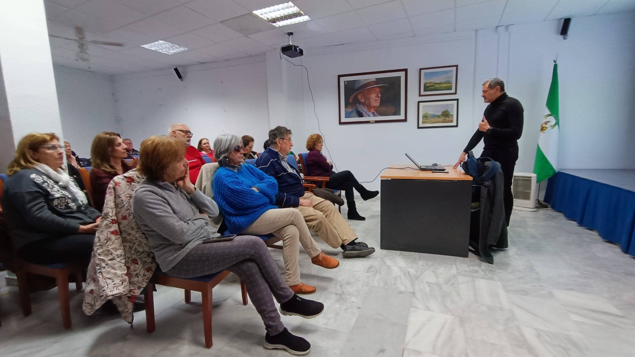 La imagen muestra a un grupo de personas sentadas en una sala durante la presentación de José Carlos Rodrigo sobre el Senior Cohousing.