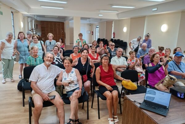 Grupo de unas 20 personas sentadas en filas frente a una mesa central y sonriendo a la cámara, durante la presentación del proyecto La Marina de Salobreña Senior Cohousing
